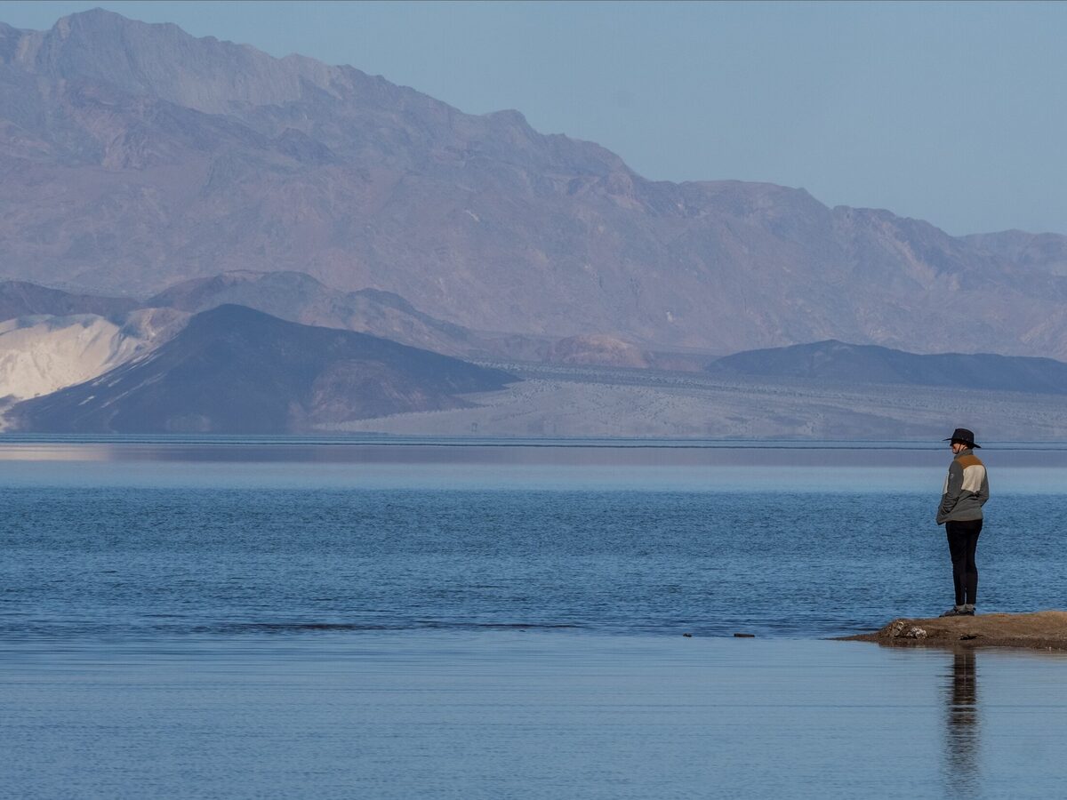 A person beside still blue water beneath desert mountains